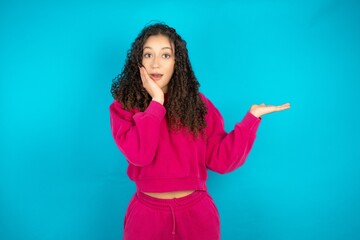Crazy Beautiful young girl wearing pink tracksuit on blue background advising discount prices hold...