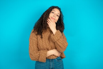 beautiful teen girl wearing brown knitted sweater laughs happily keeps hand on chin expresses positive emotions smiles broadly has carefree expression