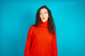 Shocked beautiful teen girl wearing red knitted sweater look empty space with open mouth screaming:...