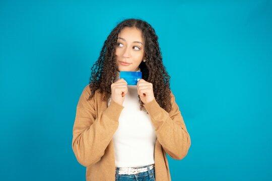 Photo of cheerful beautiful teen woman wearing beige knitted jacket hold debit card look empty space