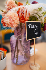 Table 6 chalked on to a small blackboard. It is a table marker in a cafe or restaurant. There are flowers in a vase behind the sign. - 700811248
