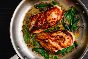 Chicken Breasts with Fresh Sage in a Stainless Steel Skillet: Marinated chicken breasts and fresh sage leaves frying in a large pan