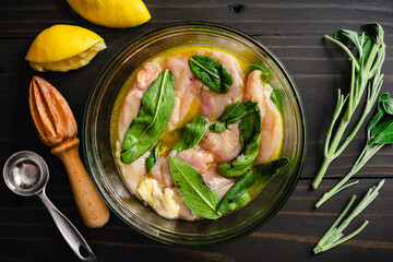 Chicken Breasts Marinating in Lemon Juice, Olive Oil, and Sage Leaves: Boneless skinless chicken breasts in a mixture of citrus, oil, and fresh herbs