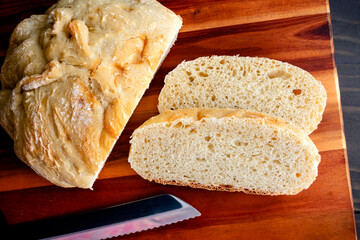 Slices of Freshly Made Crusty French Bread: Sliced loaf of homemade French bread on a wooden cutting board with a serrated bread knife