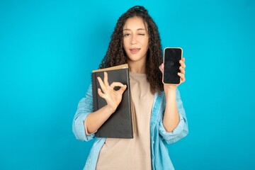 beautiful arab student carries notebooks holding in hands cell showing ok-sign