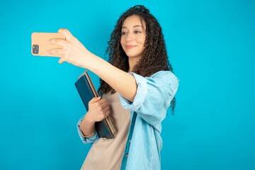 beautiful arab student carries notebooks taking a selfie to post it on social media or having a...