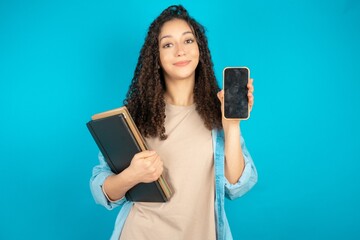 Smiling beautiful arab student carries notebooks Mock up copy space. Hold mobile phone with blank empty screen