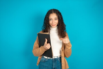 beautiful arab student carries notebooks directs fingers at camera selects someone. I recommend...