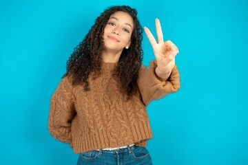 Beautiful teen girl wearing knitted sweater over blue background directs fingers at camera selects...