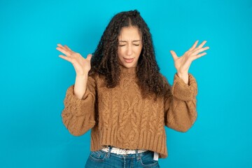 Crazy outraged Beautiful teen girl wearing knitted sweater over blue background screams loudly and...
