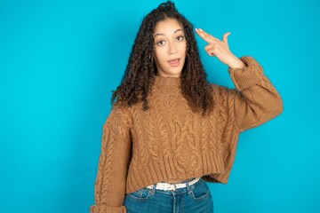 Beautiful teen girl wearing knitted sweater over blue background foolishness around shoots in...