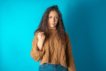 beautiful caucasian teen girl wearing brown sweater shows fist has annoyed face expression going to revenge or threaten someone makes serious look. I will show you who is boss - obrazy, fototapety, plakaty