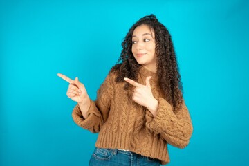 Optimistic beautiful caucasian teen girl wearing brown sweater points with both hands and  looking at empty space.