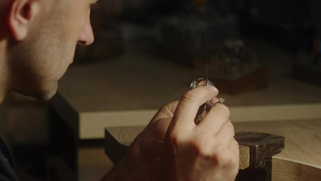 Vintage Jeweler Inspecting Ring through Loupe in Dark Workshop