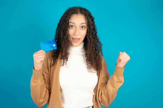 Photo of lucky impressed beautiful caucasian teen girl wearing brown sweater arm fist holding credit card. Celebrated