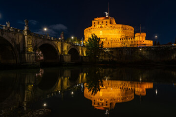 Night view of the Castel Sant'Angelo fortress and the Sant'Angelo bridge reflected in the Tiber river