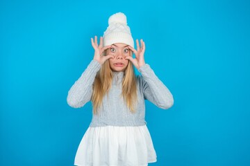 Teen caucasian girl wearing blue knitted sweater and woolly hat keeping eyes opened to find a success opportunity.