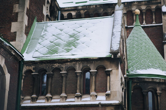 Old semicircular Gothic windows with small columns on the brown facade of a building with green kershes in the snow. Baroque and Gothic architecture. Church of Saints Olga and Elizabeth. Lviv, Ukraine