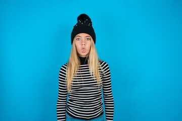 Teen caucasian girl wearing striped sweater and woolly hat making fish face with lips, crazy and...