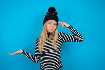 Teen caucasian girl wearing striped sweater and woolly hat confused and annoyed with open palm...