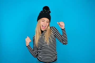 Ecstatic Teen caucasian girl wearing striped sweater and woolly hat shout loud yeah fist up raise...