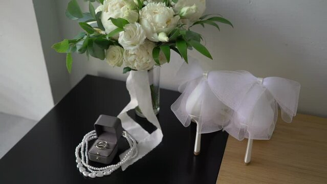 A bouquet of white peony flowers and woman shoes on a chair. Wedding rings in box. Bride's accessories in wedding day.