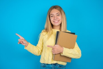 beautiful caucasian teen girl wearing yellow sweater points at copy space indicates for advertising gives right direction