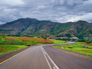 Winding road through lush Lesotho with agricultural land and mountain surrounding the valley