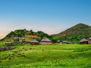 Romote village with traditional rondavel houses surrounded by lush green hills, Lesotho