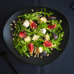 Salad with figs, arugula, nuts and cheese, topped with oil on a black plate.