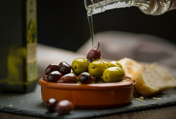 Stirred olives drizzled with olive oil from a corrugated bottle.