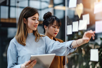 Two Women Looking at Sticky Notes on a Glass Wall