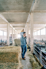 Dad with a little girl on his shoulders stands at the fence of the pen and looks at the goats. Side view