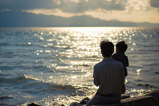 Un papa et son fils de dos, faisant face à la mer. Nature, eau, extérieur, horizon. Famille, enfant, père, garçon. Pour conception et création graphique.