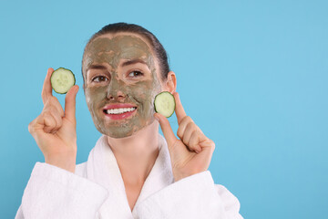 Beautiful woman with clay mask holding pieces of cucumber on light blue background, space for text