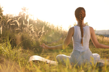 Woman practicing Padmasana on yoga mat outdoors on sunny day, back view. Lotus pose