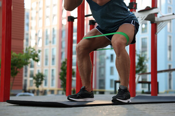 Muscular man doing exercise with elastic resistance band on mat at sports ground, closeup