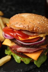 Delicious burger with meat cutlets, bacon, cheese, vegetables and lettuce on black table, closeup