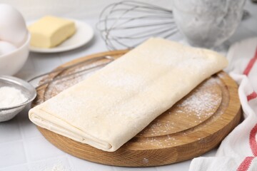 Obraz na płótnie Canvas Raw puff pastry dough on white tiled table, closeup