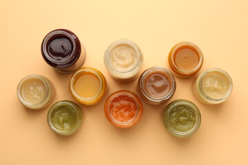 Jars with healthy baby food on pale orange background, flat lay