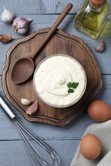 Tasty mayonnaise in bowl, ingredients and whisk on gray wooden table, flat lay