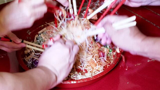 Perspective view of people mixing and tossing yusheng or yee sang during Chinese New Year dinner celebration.