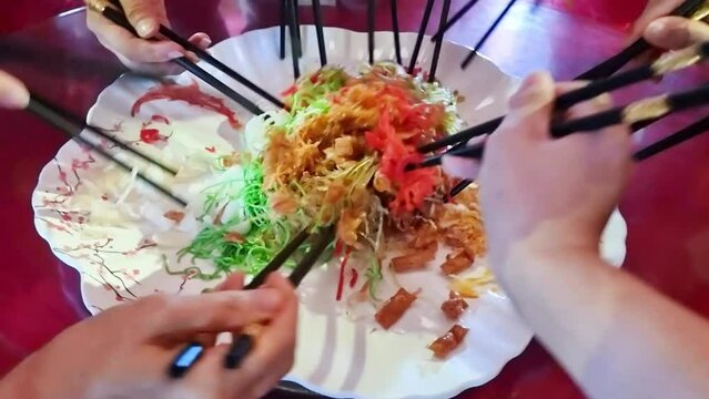 Perspective view of people mixing and tossing yusheng or yee sang during Chinese New Year dinner celebration.