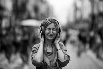 Close-up of a woman listening to headphones on a busy street. Black and white photo.