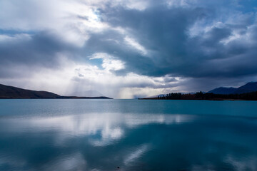 Photograph of early morning sun shining through rain clouds on Lake Tekapo on the South Island of...