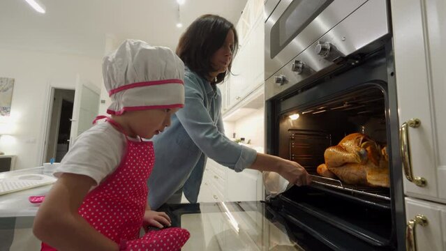 mother and child cooking roasted stuffed turkey in kitchen oven, thanksgiving and christmas holiday dinner