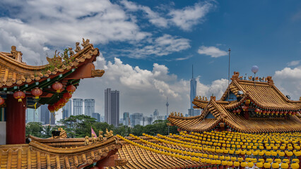 The roofs of a Chinese temple against a blue sky, clouds and modern city skyscrapers. Figures of...