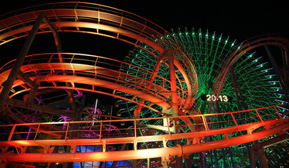 Steel-framed building illuminated by colorful lights of amusement park at night