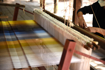 Women's hands weaving silk on a traditional wooden loom.