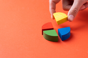 Colorful wooden pie chart pieces, fingers adding piece of diagram